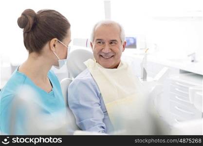Female dentist talking to smiling senior patient at dental clinic
