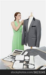 Female designer adjusting coat on tailor&acute;s dummy over gray background