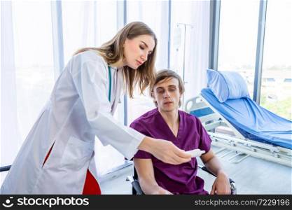 female doctor and checking man patient&rsquo;s sit in a wheelchair Look at temperature with Tympanic Thermometer on Bed with Digital pressure gauge for better healing In the room hospital background.