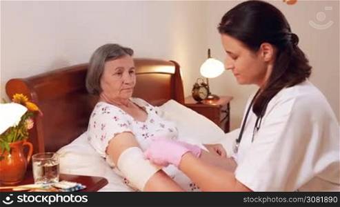 Female doctor bandages senior woman elbow at home. Medicine, age, support, health care and people concept - doctor caring senior patient. Slow motion