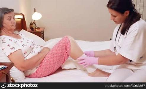 Female doctor bandages senior woman leg at home. Medicine, age, support, health care and people concept - doctor caring senior patient. Slow motion