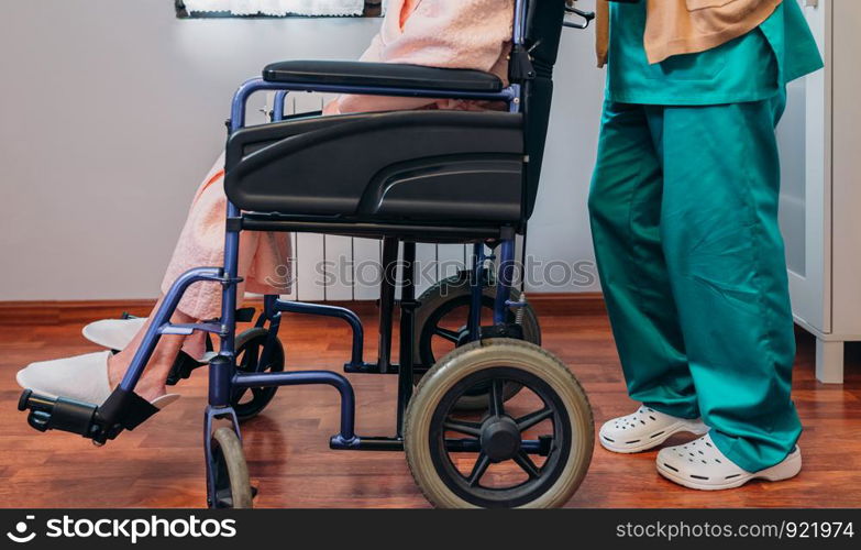 Female doctor carrying elderly female patient in a wheelchair. Doctor carrying elderly patient in a wheelchair