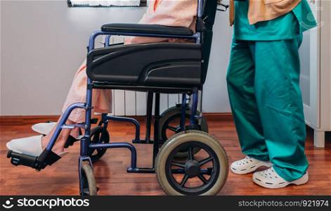 Female doctor carrying elderly female patient in a wheelchair. Doctor carrying elderly patient in a wheelchair