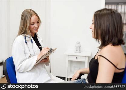 Female doctor explaining diagnosis to her patient. Brunette woman having consultation with smiling blonde girl in medical office.