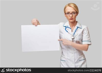 Female doctor holding a blank banner sign standing over grey background.. Female doctor holding a blank banner sign standing over grey background