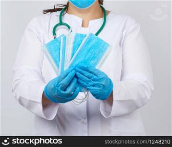 female doctor in a white coat and mask holds a stack of protective face masks about the virus, doctor stands on a white background, place for an inscription