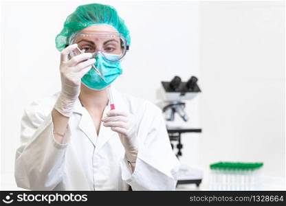 Female doctor in the laboratory with a blood tube for analysis and sampling of Coronavirus under the microscope .. Female doctor in the laboratory with a blood tube for analysis and sampling of Coronavirus under the microscope.