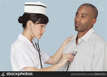 Female doctor listening the heartbeat of male patient over light blue background
