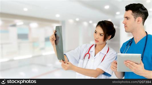 Female doctor looking at x ray film while discussing with another doctor holding a tablet computer at the hospital. Medical healthcare staff and doctor service.