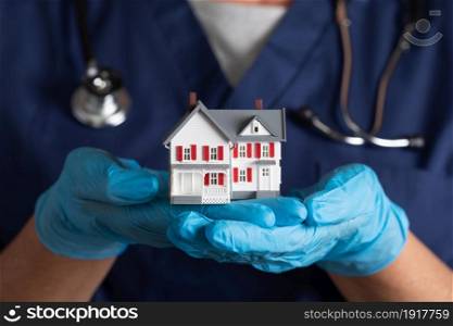 Female Doctor or Nurse Wearing Surgical Gloves Holding Model Home.