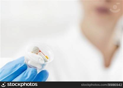 Female doctor s hand In blue glove holding graduated medicine cups full of pills. Copy space and white background.. Doctor s Hand in a Glove Holding Graduated Medicine Cups with Pills