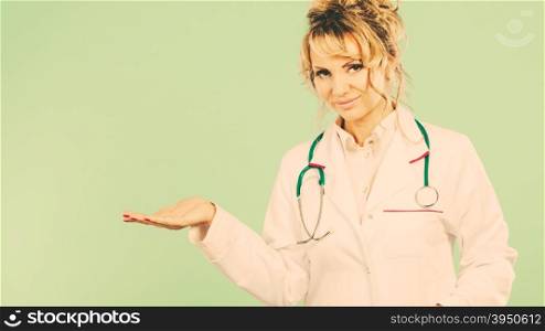 Female doctor showing copy space.. Female medical doctor showing copy space. Woman in white professional uniform with stethoscope on neck invite people to clinic hospital. Middle aged pharmacist nurse on green.