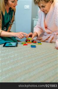 Female doctor showing geometric shape game to elderly female patient with dementia. Female doctor showing geometric shapes to elderly patient