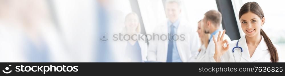 Female doctor showing Ok sign , team of doctors on background. Female doctor showing Ok sign
