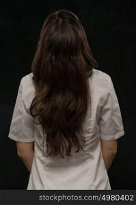 Female doctor standing in front of black background. Photo from behind
