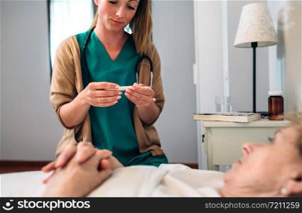 Female doctor taking temperature to senior woman at home. Doctor taking temperature to senior woman
