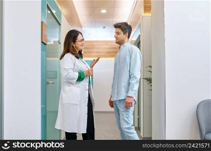 Female doctor talking to male patient. Physician explaining something to young man in corridor. Female doctor discussing something with male patient