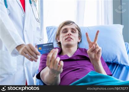 Female doctor therapeutic advising and a man patient on bed Abstract blur with focus show holding a credit card lying with lifts two fingers up fightingin the room hospital background,payment medical