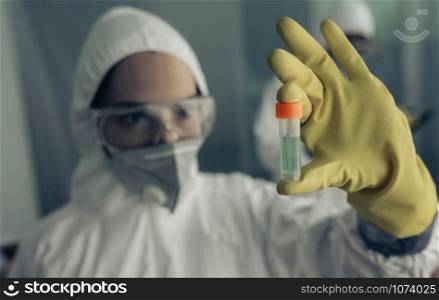 Female doctor with baceriological protective suit looking at an antidote vial for a dangerous virus. Woman with baceriological protective suit looking at an antidote vial