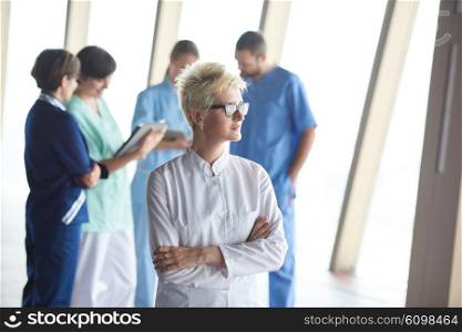 female doctor with glasses and blonde hairstyle standing in front of team in background, group of medical staff at hospital