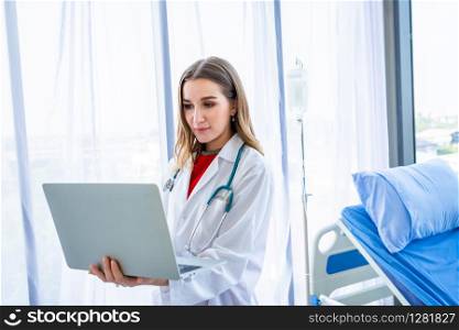 female doctor with stethoscope working with laptop computer and writing on paperwork on wooden table in Hospital background