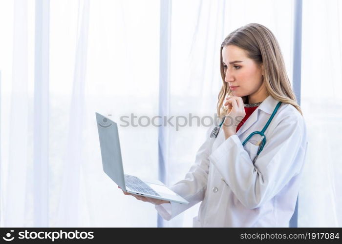 female doctor with stethoscope working with laptop computer and writing on paperwork on wooden table in Hospital background