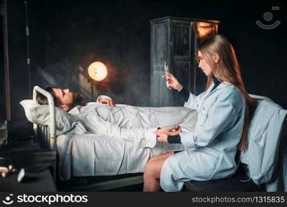 Female doctor with syringe against male patient in hospital bed. Illness of man in clinic, health recovery and treatment. Female doctor with syringe against male patient