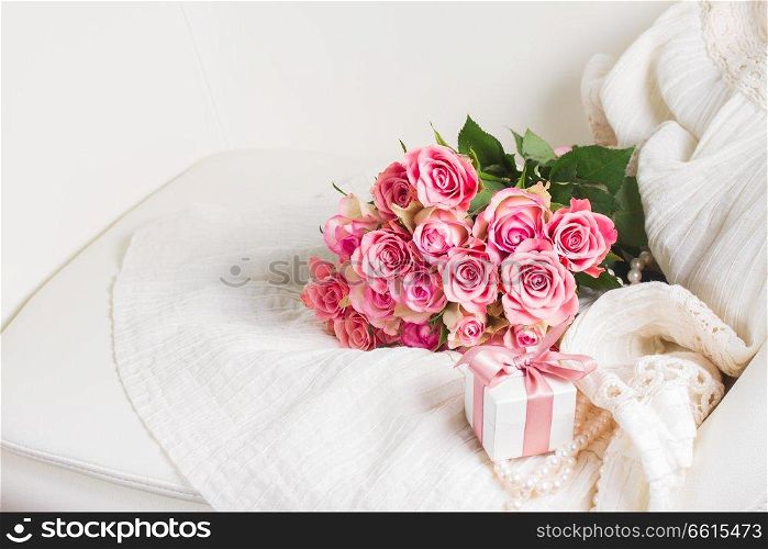 Female dress and jewellery with freah roses bouquet and gift box on chair, place for copy space. Female accessories on white