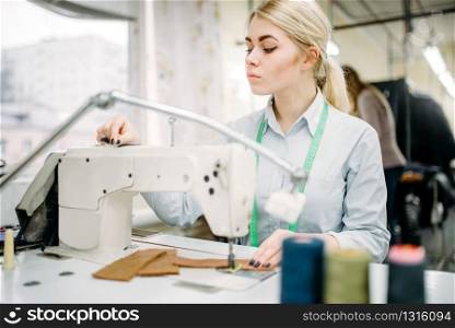 Female dressmaker sews on serger machine. Tailoring or dressmaking on clothing factory, needlework or sewing, seamstress in workshop. Female dressmaker sews on serger machine