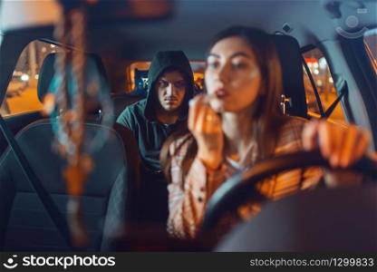 Female driver and hooded car burglar on back seat, criminal lifestyle, stealing. Male bandit and victim in vehicle on parking. Auto robbery, automobile crime, hijacking