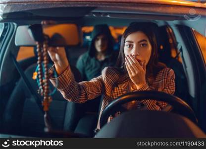 Female driver and hooded car hijacker on back seat, criminal lifestyle, stealing. Male bandit and victim in vehicle on parking. Auto robbery, automobile crime, hijacking