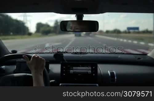 Female driver driving car on high speed freeway on sunny day with blurred busy traffic on background. View from inside out of vehicle&acute;s interior.