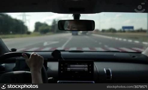 Female driver driving car on high speed freeway on sunny day with blurred busy traffic on background. View from inside out of vehicle&acute;s interior.
