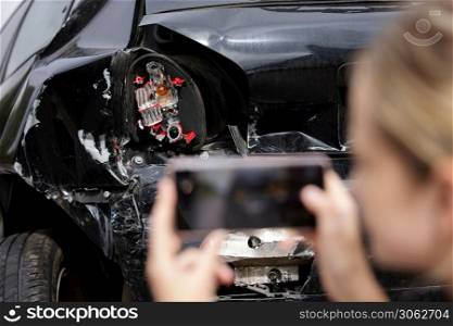 Female Driver Taking Photo Of Damaged Car After Accident For Insurance Claim On Mobile Phone