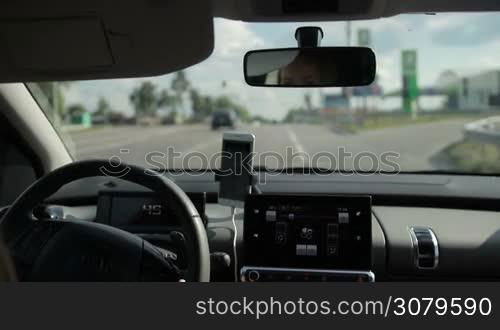 Female driver turning to petrol station to refuel the car. View from inside of auto. Beautiful female driver driving vehicle on highway and going to modern gas station on sunny day.