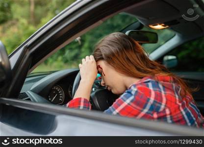 Female driver with blooded face sitting in the car after accident on road. Automobile crash, blood on the woman&rsquo;s face. Broken automobile or damaged vehicle, auto collision on highway