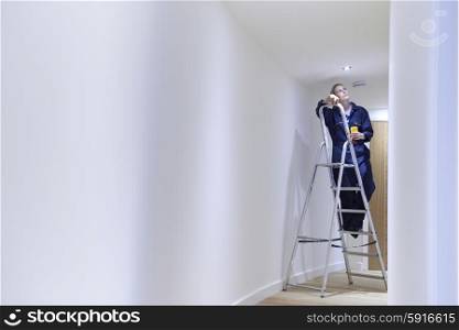 Female Electrician Installing Lights In Ceiling