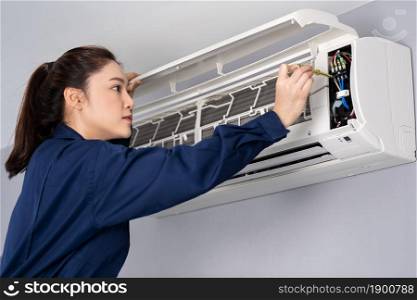 female electrician with screwdriver repairing the air conditioner indoors
