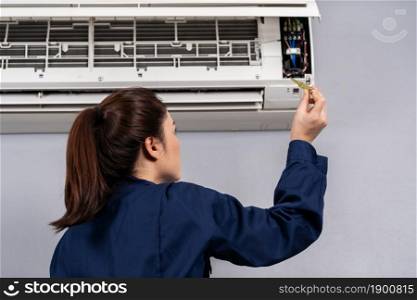 female electrician with screwdriver repairing the air conditioner indoors
