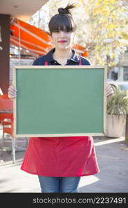 female entrepreneur holding blank green menu board outdoors caf