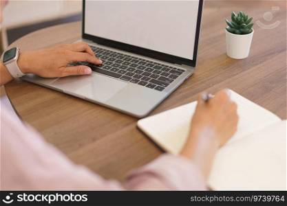Female entrepreneur working at home to searching business data on laptop and writing notes in paper.