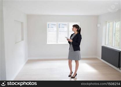 Female Estate Agent With Digital Tablet Looking Around Vacant Property For Valuation