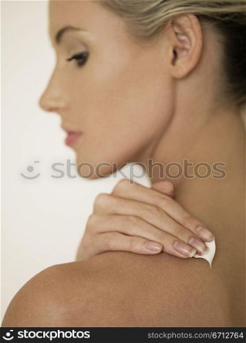 female face in profile rubbing cream into shoulder