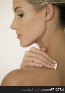 female face in profile rubbing cream into shoulder