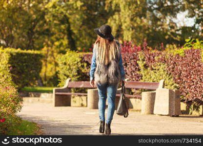 Female fashion. Back view of attractive long haired model wearing stylish clothes in park. Fashionable young model spending time on air. . Back view of stylish woman on air