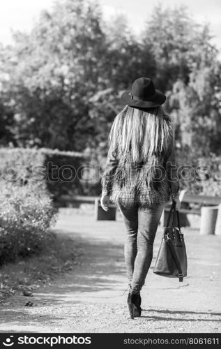 Female fashion. Back view of attractive long haired model wearing stylish clothes in park. Fashionable young model spending time on air.