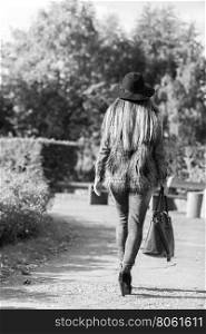 Female fashion. Back view of attractive long haired model wearing stylish clothes in park. Fashionable young model spending time on air.