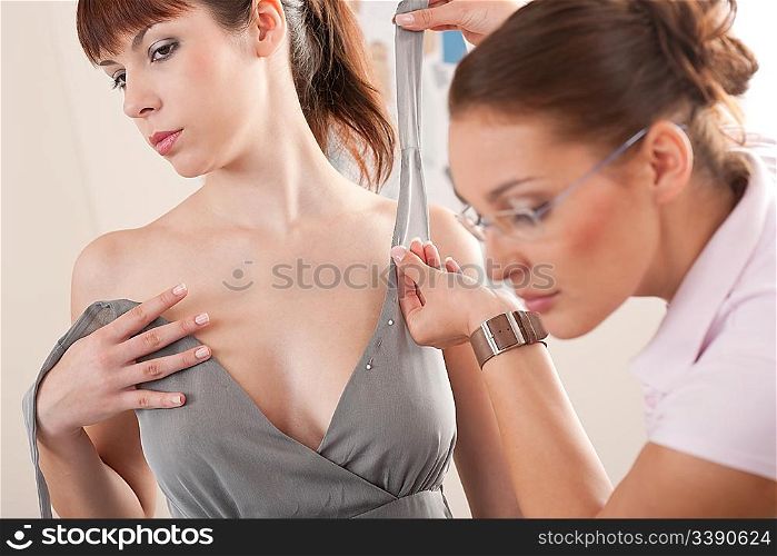 Female fashion designer pinning gray dress on model in studio