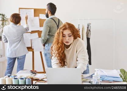 female fashion designer working atelier with colleagues laptop