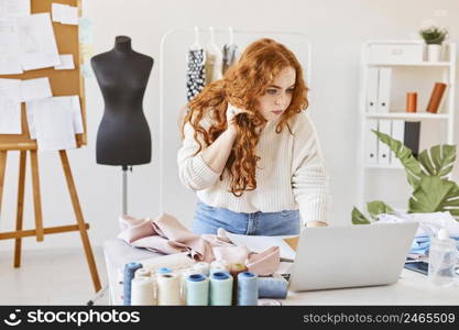 female fashion designer working atelier with laptop talking smartphone